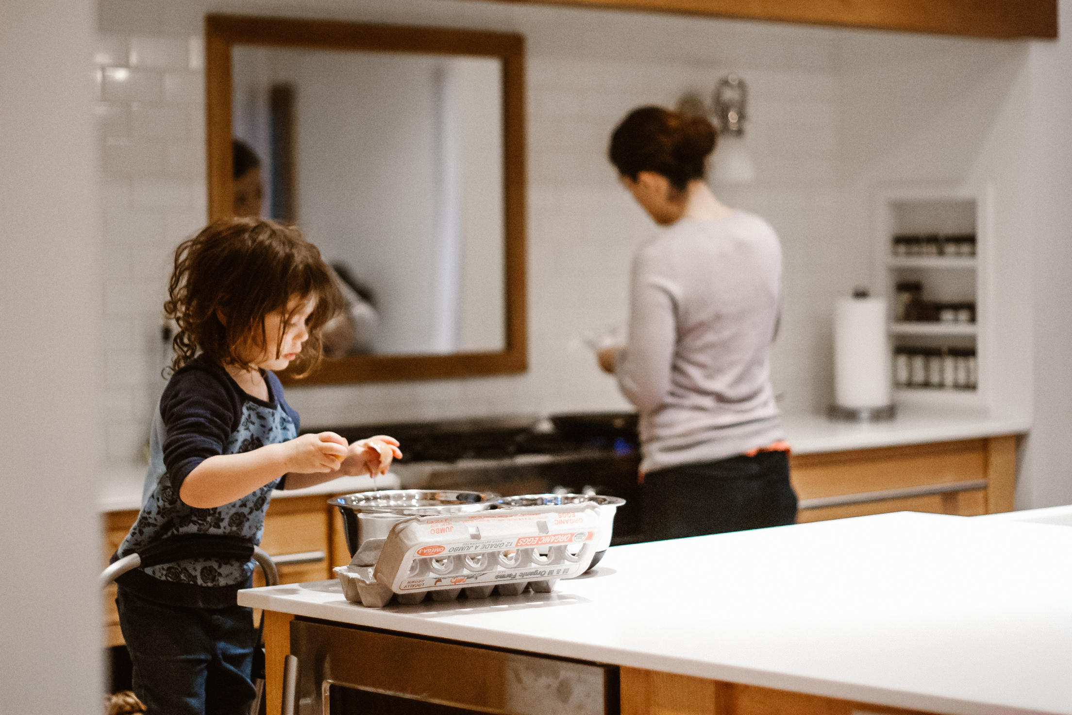 Little girl in the kitchen helping mom cook breakfast by cracking eggs.
